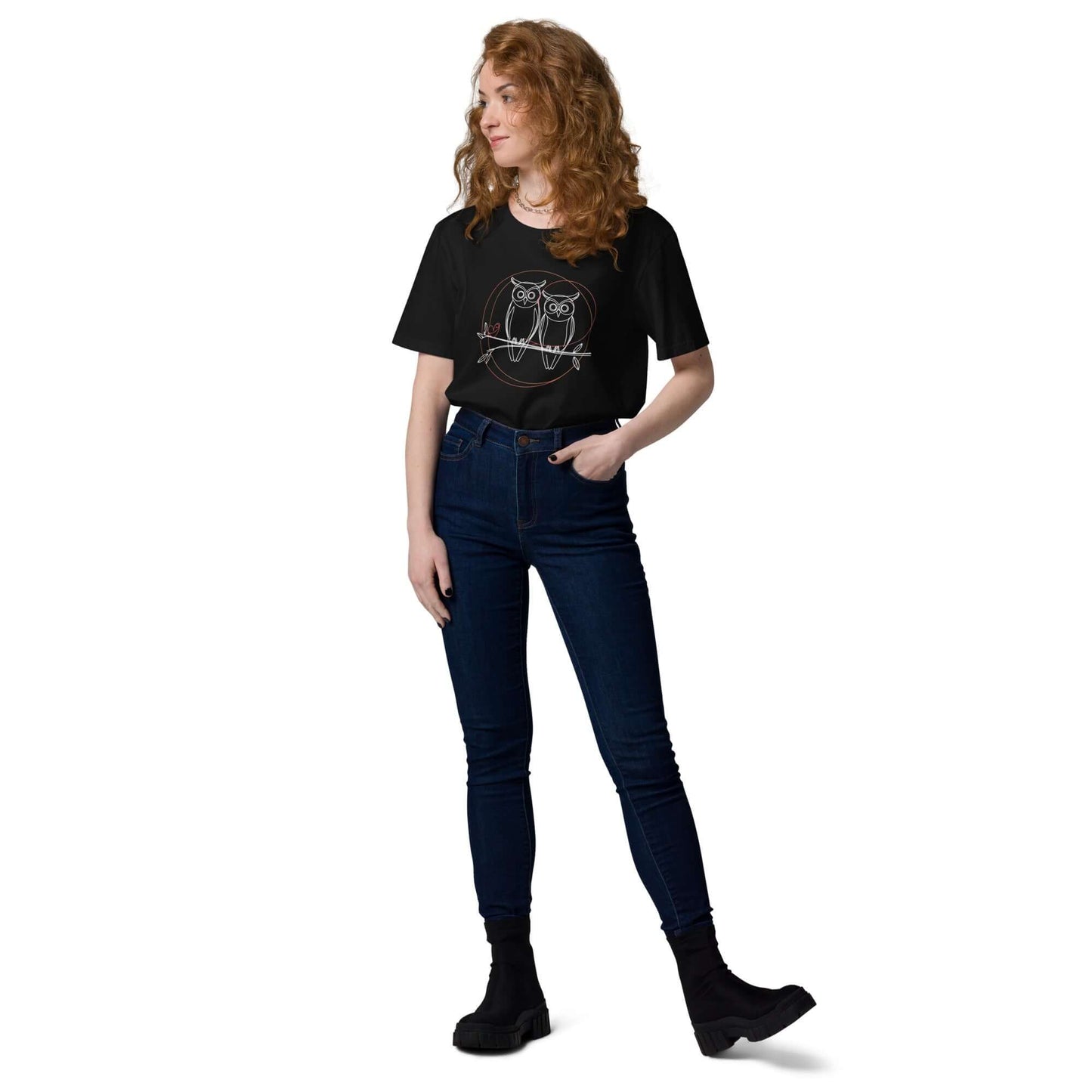 Woman wearing a black owl-themed unisex organic cotton t-shirt with high-waisted jeans and black boots.